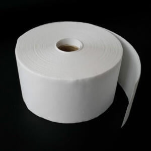 A large, white, unspooled roll of toilet paper against a dark background. The end of the roll is slightly unrolled and hanging down. The paper appears smooth and thick, and the cardboard core is visible.