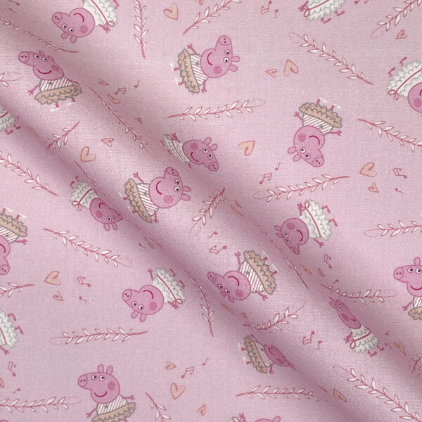 A piece of pink fabric with a repetitive pattern featuring a cartoon character dressed as a ballerina. The character is surrounded by small decorative elements like hearts and musical notes. The fabric is slightly wrinkled, showing texture and folds.