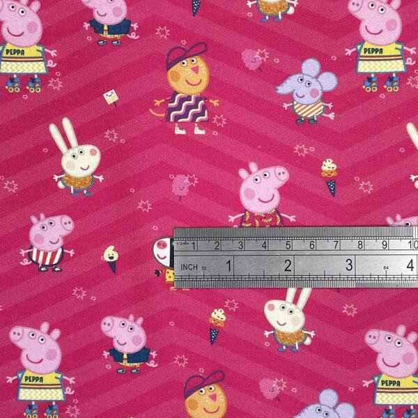 A vibrant pink fabric with cartoon characters including pigs, a rabbit, a mouse, and a humanoid figure, all wearing colorful clothes. Ice cream cones are scattered across the fabric. A metal ruler measuring 6 inches is placed on the fabric for scale.