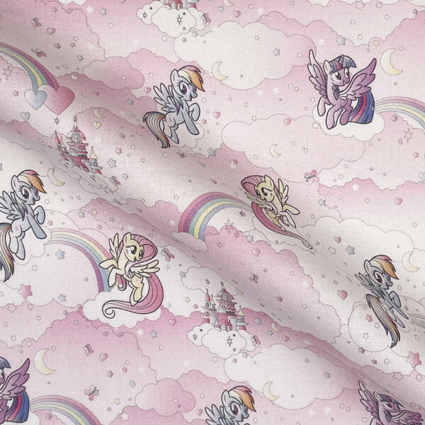 A fabric with a light pink background features colorful ponies with wings, rainbows, clouds, crescent moons, hearts, and castles. The ponies are in various poses and have wings and different mane colors. The scene is whimsical and childlike.