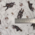 A fabric with a repeating pattern of two characters: one in armor with a cape and the other small, wearing robes. The characters are oriented in various positions. A metal ruler is placed horizontally across the fabric for scale.