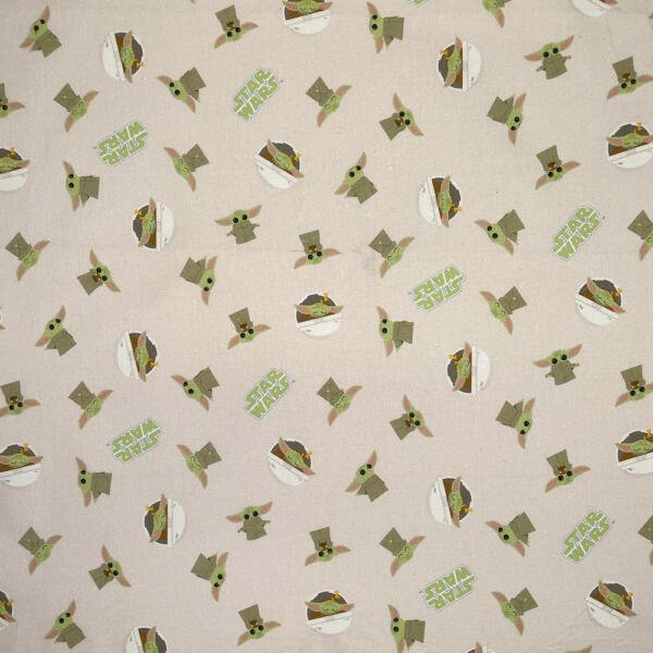 A fabric with a repeating pattern of green cartoon baby aliens with large ears, some in a floating pod, and "Star Wars" text in green. The background is a light beige color.