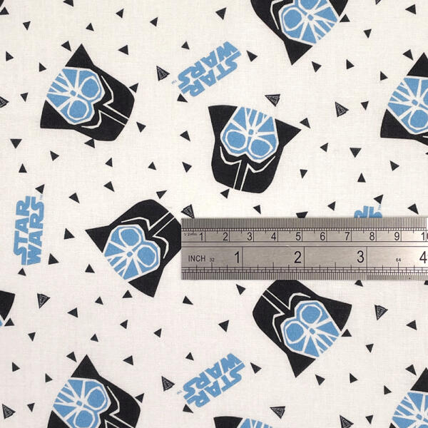A white fabric patterned with black helmets resembling Darth Vader from Star Wars, featuring blue accents. Scattered among the helmets are small black triangles and the blue text "Star Wars." A metal ruler is placed on the fabric, showing measurements in inches and centimeters.