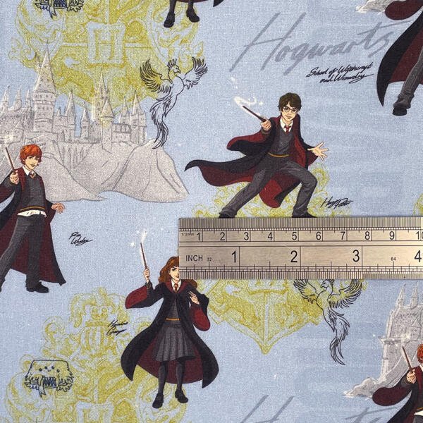 Fabric with Harry Potter-themed design featuring characters holding wands, a castle, and a ruler laid on top for scale. The background includes a light blue backdrop with subtle magical elements, including crests and mystical creatures.
