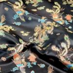 A close-up view of luxurious black fabric featuring intricate, multicolored embroidery. The embroidered pattern includes mythical creatures such as dragons and phoenixes, along with floral elements, showcasing vibrant hues of gold, blue, and red.