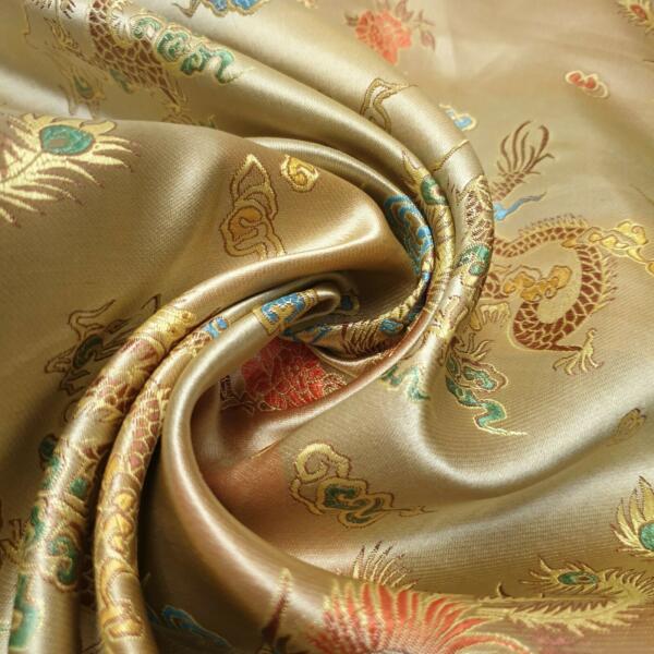 A close-up image of luxurious gold silk fabric intricately embroidered with colorful dragons and floral motifs. The fabric is artfully draped and gently twisted, showcasing its smooth texture and elaborate design.