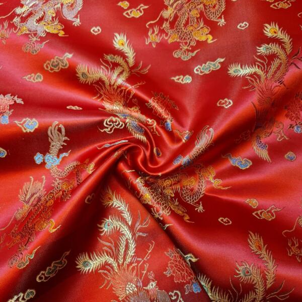 Close-up of a vibrant red silk fabric adorned with intricate gold dragon motifs and cloud patterns. The fabric has a shiny finish and appears gently wrinkled at the center, highlighting its texture and the detailed weaving of the designs.