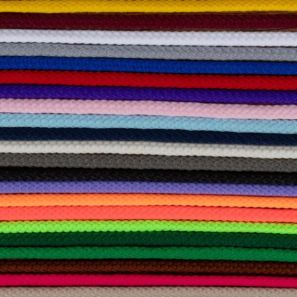 A stack of colorful braided cords arranged horizontally in rows. Colors include red, yellow, white, blue, purple, pink, black, gray, brown, green, orange, and more. Each cord's intricate braided pattern is visible, creating a textured and vibrant visual.