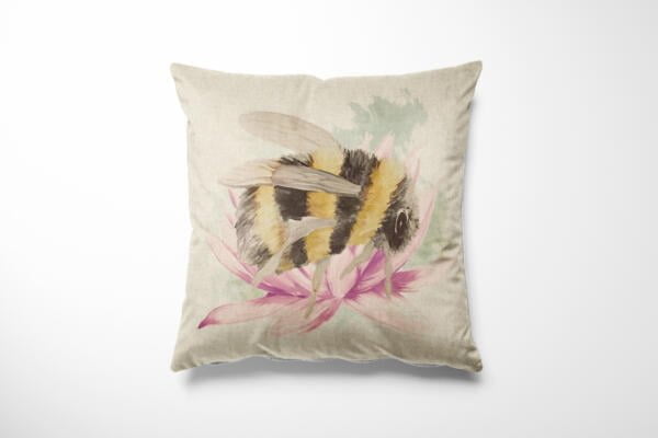 A beige square throw pillow featuring an illustration of a bumblebee perched on a pink flower. The design emphasizes the bee's yellow and black stripes and the delicate petals of the flower. The background is light and neutral, highlighting the detailed artwork.