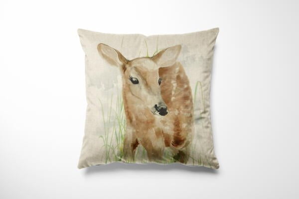 A square cushion features a watercolor-style illustration of a young deer amid grass, set against a light beige background. The deer, depicted with soft brown shades and delicate details, creates a serene and nature-inspired design on the cushion.