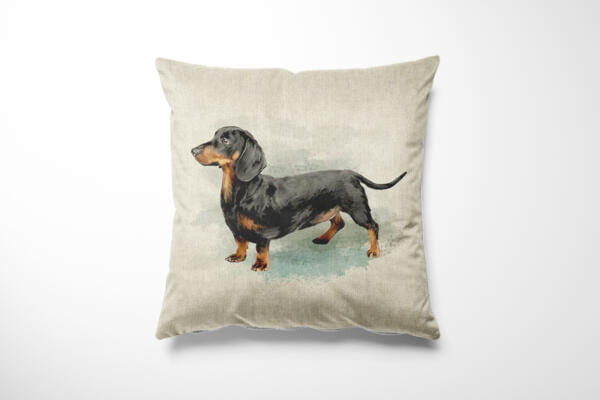 A square cushion with a light beige background features an illustration of a black and brown dachshund standing upright. The dog is looking to the left with its tail slightly raised. The cushion is set against a plain white backdrop.