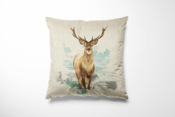 A square throw pillow with a beige background featuring a realistic illustration of a stag with large antlers standing in a natural, misty landscape. The design is centered on the pillow and showcases the stag facing forward.