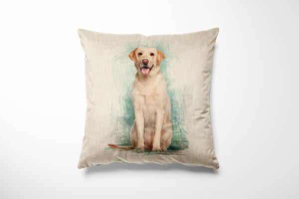 A beige cushion with an artistic illustration of a light brown Labrador Retriever sitting and facing forward. The dog is smiling with its tongue out, set against a subtle greenish-blue watercolor background. The cushion has a plain white background.