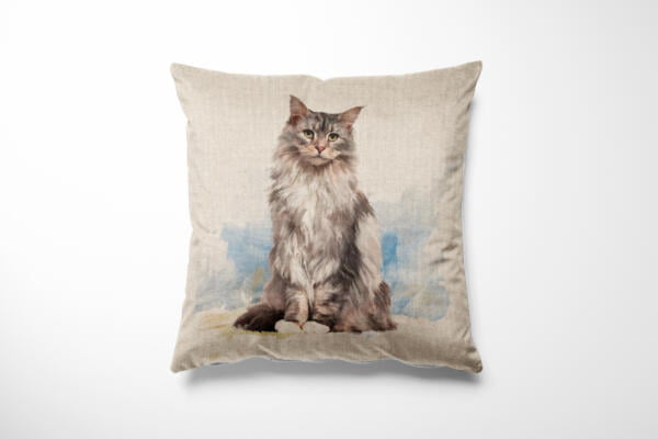 A square throw pillow features a realistic, detailed illustration of a long-haired gray cat. The cat is positioned sitting upright against a soft, muted background. The pillow itself appears to be made of a textured, beige fabric.