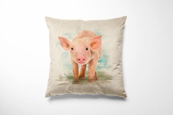 A decorative pillow features a realistic painting of a piglet with a light beige background. The piglet has pink ears, a snout, and is standing on green grass, creating a soft, charming, and cozy appearance.