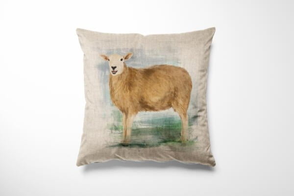 A square beige cushion features a detailed illustration of a standing sheep on it. The background of the image is a soft blur of green and blue hues, adding a subtle contrast to the cushion's design. The sheep is looking directly forward.