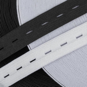 Close-up image of two elastic bands, one black and one white, on a textured gray and black circular background. Each band features small, regularly spaced rectangular openings. The background has a ribbed texture that adds depth to the image.