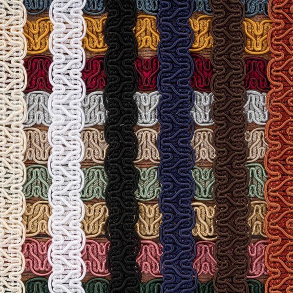 Close-up of intricately woven, colorful braided cords arranged vertically in rows. Each row features a different color, including white, yellow, red, green, black, blue, brown, and various other shades. The texture and patterns of the braids are prominent.