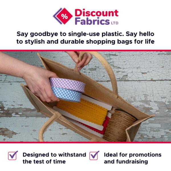 A hand is placing a round container into a reusable shopping bag on a distressed wooden surface. The banner reads "Discount Fabrics LTD" and promotes durable shopping bags for life. It emphasizes the bags' longevity and suitability for promotions and fundraising.