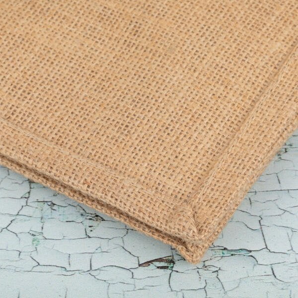 Close-up photo of two pieces of burlap fabric with stitched edges, layered one over the other, placed on a surface with a cracked, light blue paint texture.