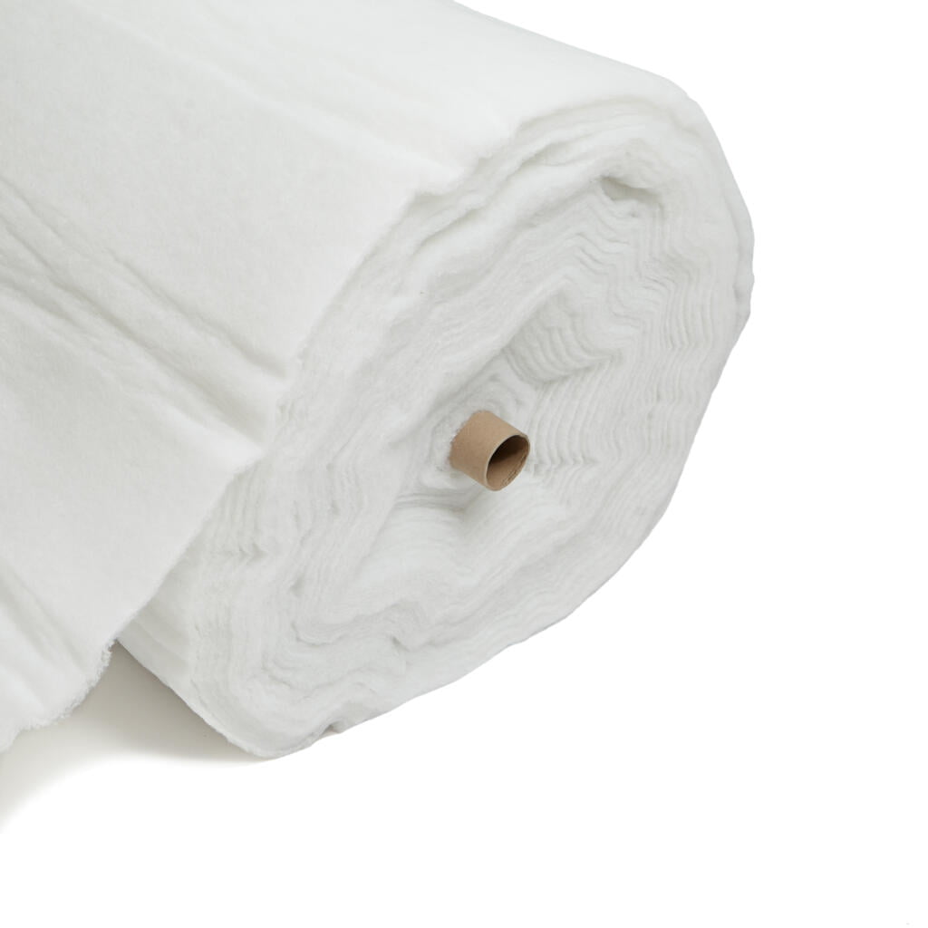 A large roll of white, fluffy batting material is shown against a plain white background. The roll is partially unrolled, revealing the soft, fibrous texture of the material, with a cardboard tube at the center.