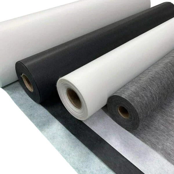 A close-up view of several rolls of fabric or non-woven material. The rolls are aligned horizontally, featuring a variety of colors including white, gray, and black. The edges of the fabrics are neatly cut, and the materials appear to be of different textures and thicknesses.