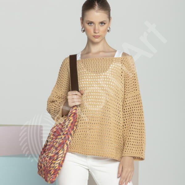 A woman with light brown hair is wearing a loose-knit beige sweater and white pants, holding a multicolored woven shoulder bag. She stands against a light-colored background, looking directly at the camera with a neutral expression.