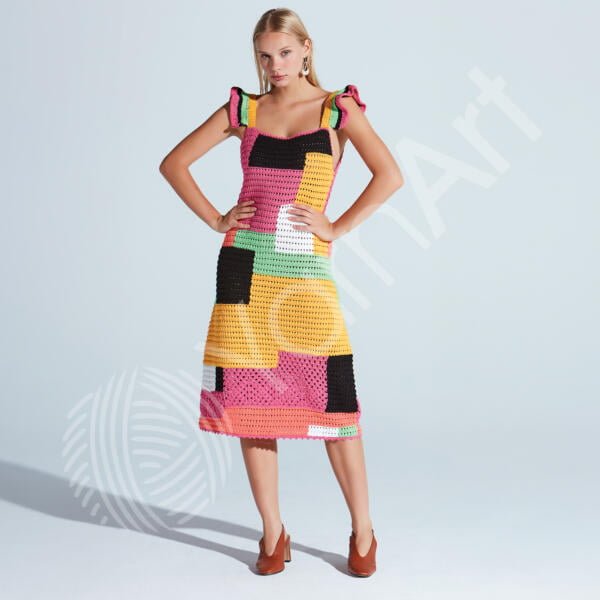 A woman stands confidently modeling a colorful, patchwork-style, mid-length dress with shoulder straps. The dress features various blocks of colors, including pink, yellow, black, green, and orange. She pairs the dress with brown heels, posing against a light background.