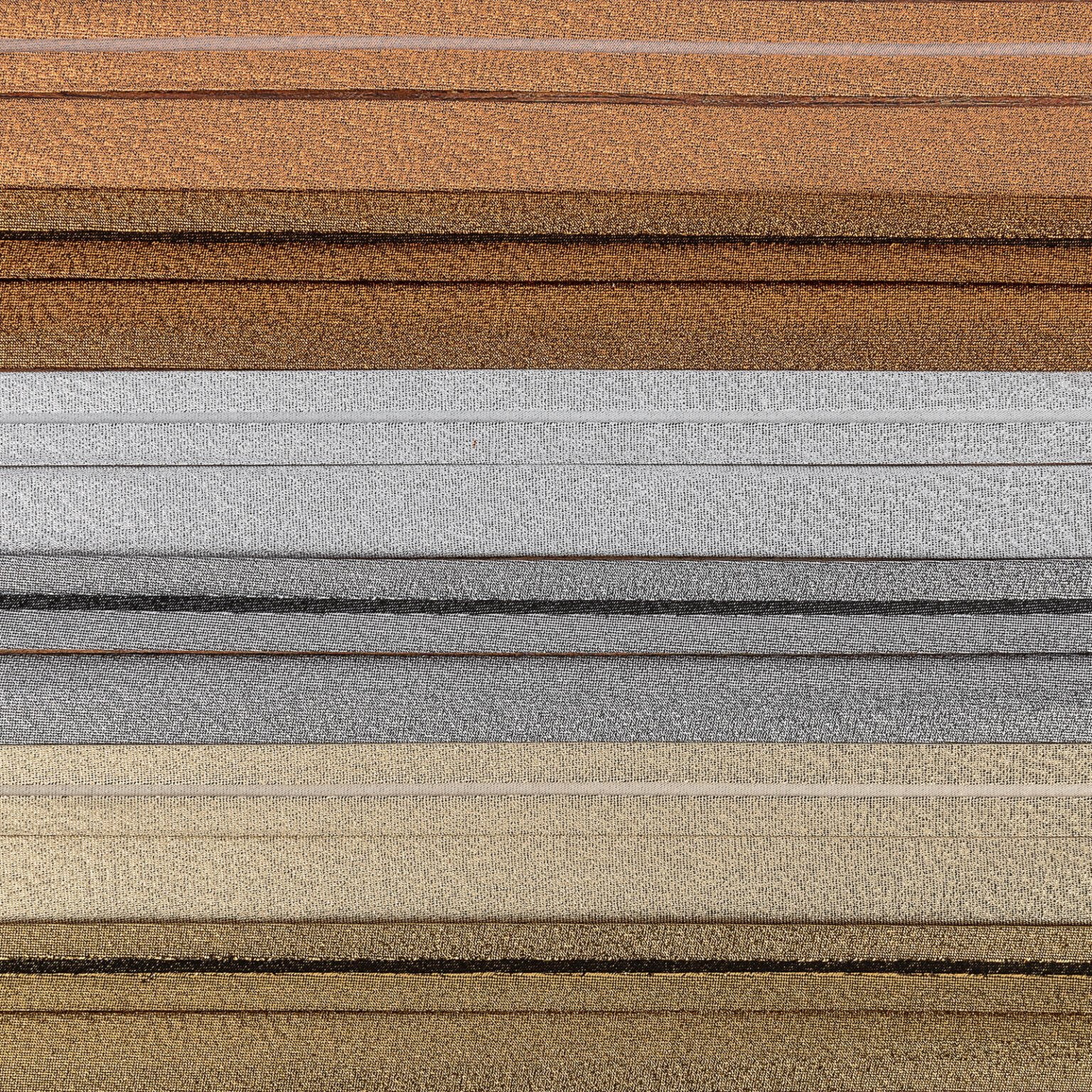 A close-up image of multiple horizontal layers of textured fabric in various shades, including brown, silver, gold, and gray. The fabrics are neatly stacked on top of each other, highlighting their varied colors and textures.