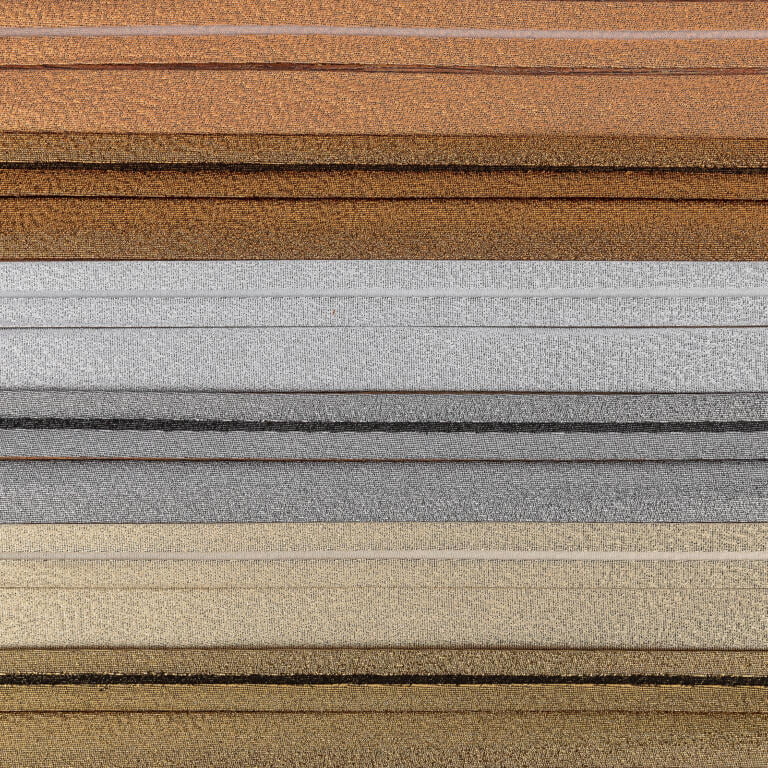 A close-up image of multiple horizontal layers of textured fabric in various shades, including brown, silver, gold, and gray. The fabrics are neatly stacked on top of each other, highlighting their varied colors and textures.