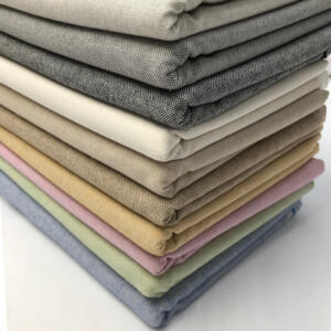 A stack of neatly folded, solid-colored fabric swatches arranged in a gradient from dark to light. The fabrics include various shades of gray, beige, cream, tan, pink, lavender, green, and blue, showcasing a range of pastel and neutral tones.