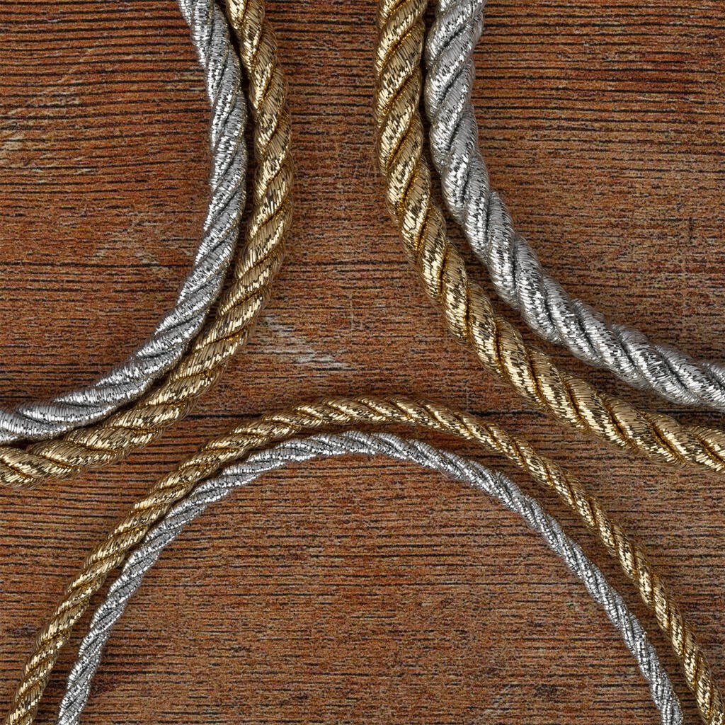 Three sections of intertwined metallic cords, two in silver and one in gold, are arranged on a textured wooden surface. The cords are neatly coiled and create an elegant contrast against the rustic background.