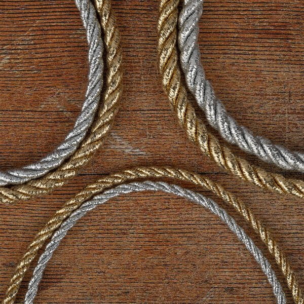 Three sections of intertwined metallic cords, two in silver and one in gold, are arranged on a textured wooden surface. The cords are neatly coiled and create an elegant contrast against the rustic background.