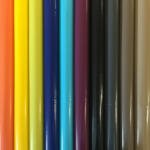 A close-up image of colorful rolls of vinyl arranged vertically. The colors, from left to right, include bright red, orange, light orange, yellow, bright yellow, blue, cyan, turquoise, purple, black, dark grey, grey, light grey, and white.