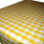 A table covered with a yellow and white checkered tablecloth featuring a classic gingham pattern. The tablecloth appears clean and neatly spread, with the checkered squares evenly aligned. The edge of the table is visible in the background.