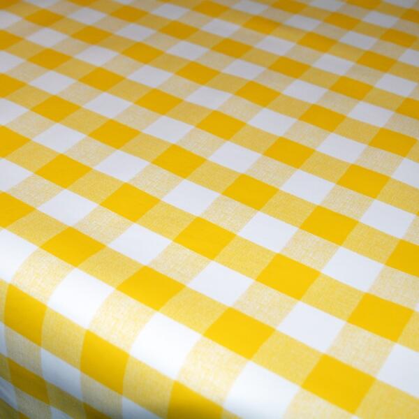 A close-up image of a table covered with a yellow and white gingham tablecloth. The pattern features alternating yellow and white squares in a classic checkered design. The tablecloth appears to be neatly spread across the surface.