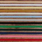 A collection of various colorful lace trims arranged in horizontal rows. The laces are in shades of brown, yellow, green, blue, pink, and other colors, each featuring intricate patterns and designs.
