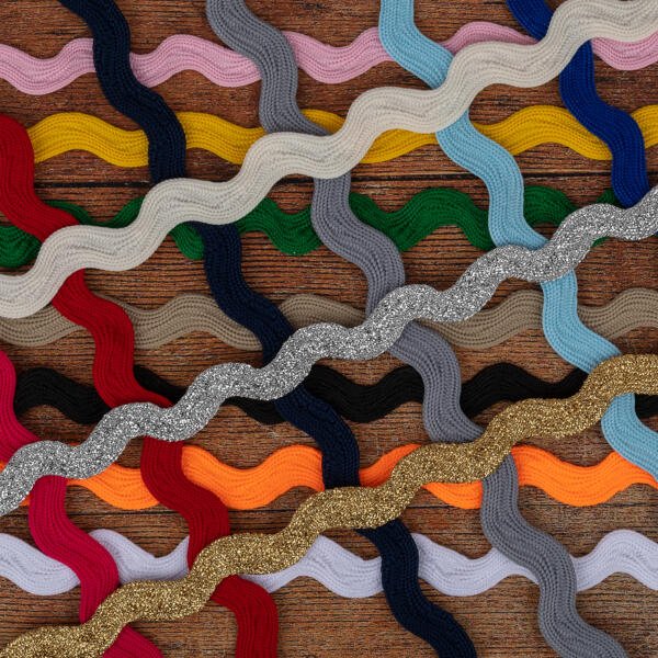 A series of wavy, colorful ribbons arranged parallel to each other on a wooden surface. The ribbons come in various colors, including red, yellow, green, blue, gray, black, and gold, with some featuring a glittery texture.