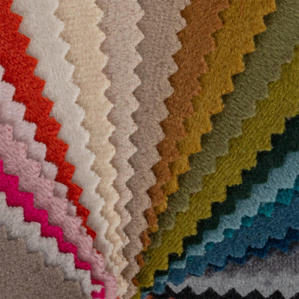 A close-up view of fabric swatches arranged in a fan shape. The swatches display various colors, including shades of brown, red, orange, green, blue, pink, and gray, with a zigzag edge pattern. The texture appears to be soft and plush.