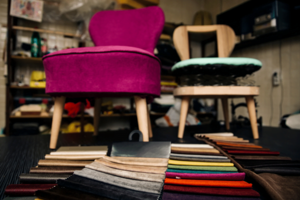 Image showing different fabrics on the floor next to a vintage chair that can be used for reupholstery. From velvet fabric to faux leather fabric