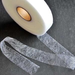 A roll of lightweight white interfacing tape is unwound on a dark surface. The translucent material appears textured and is used in sewing and crafting for reinforcing fabric.