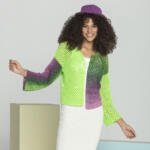 A woman with curly hair smiles, wearing a colorful crochet outfit. She has on a hat and a jacket that transitions from green to purple, paired with a white dress. She poses in front of a minimalist, neutral-colored backdrop.