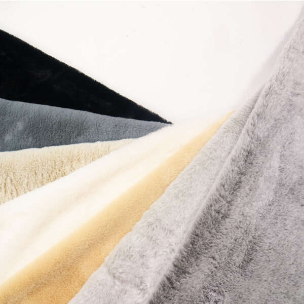 A variety of soft, plush fabric samples are fanned out. They showcase different colors, including black, gray, off-white, beige, and light gray, all resting on a white surface. The textures appear smooth and fluffy, suggesting a cozy material.
