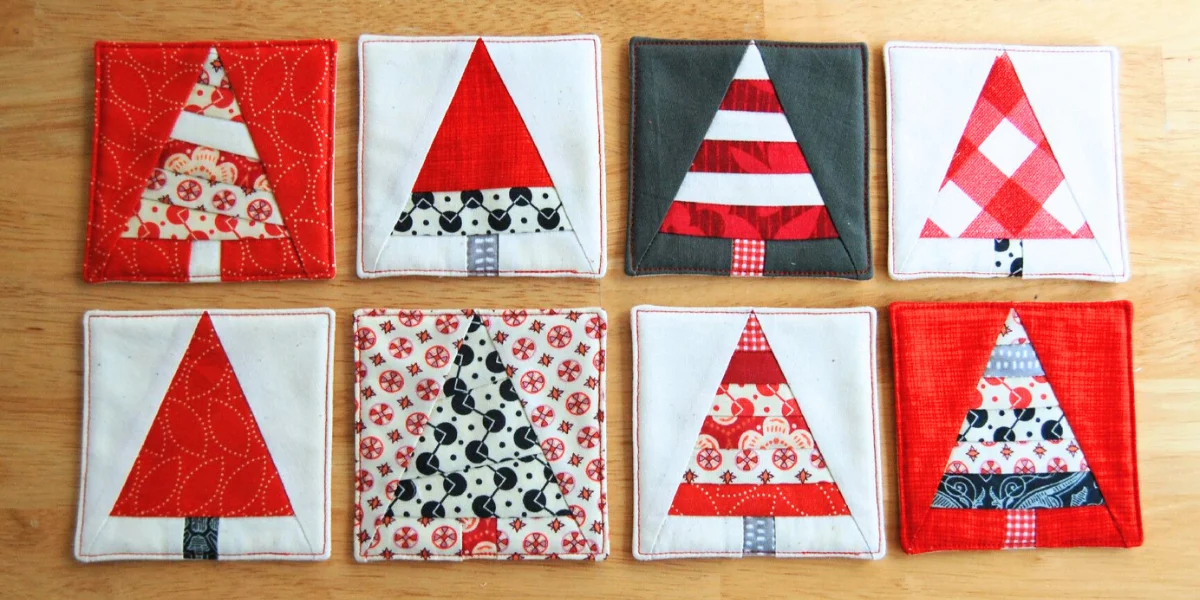 Eight quilted fabric coasters with Christmas tree designs. The trees are in red, white, and patterned fabrics on various backgrounds – four on top and four below. The background colors are red, grey, white, and patterned with holiday themes.