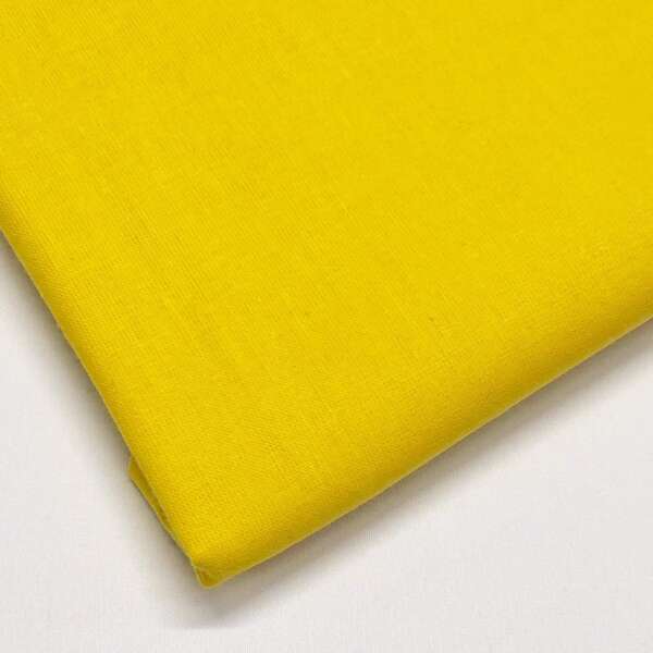 A neatly folded piece of bright yellow fabric lies against a white background, showcasing its smooth texture and vibrant color. The edge of the fabric is angled towards the lower left corner of the image.