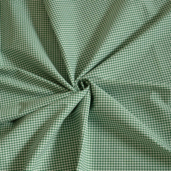 A piece of green and white gingham fabric is laid out, with the center gathered into a swirl pattern. The fabric features a small, repetitive checkered design typical of gingham. The folds create shadows and texture, enhancing the fabric's detail.