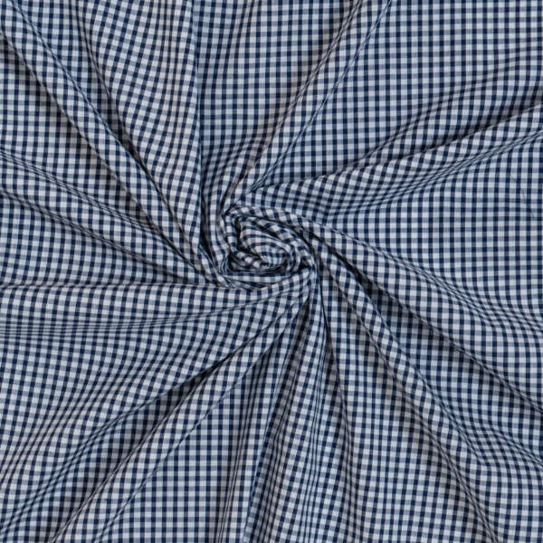 A piece of blue and white gingham fabric is tightly gathered and twisted into a circular pattern in the center, creating radiating folds. The checkered pattern is consistent throughout, giving a neat and uniform appearance.