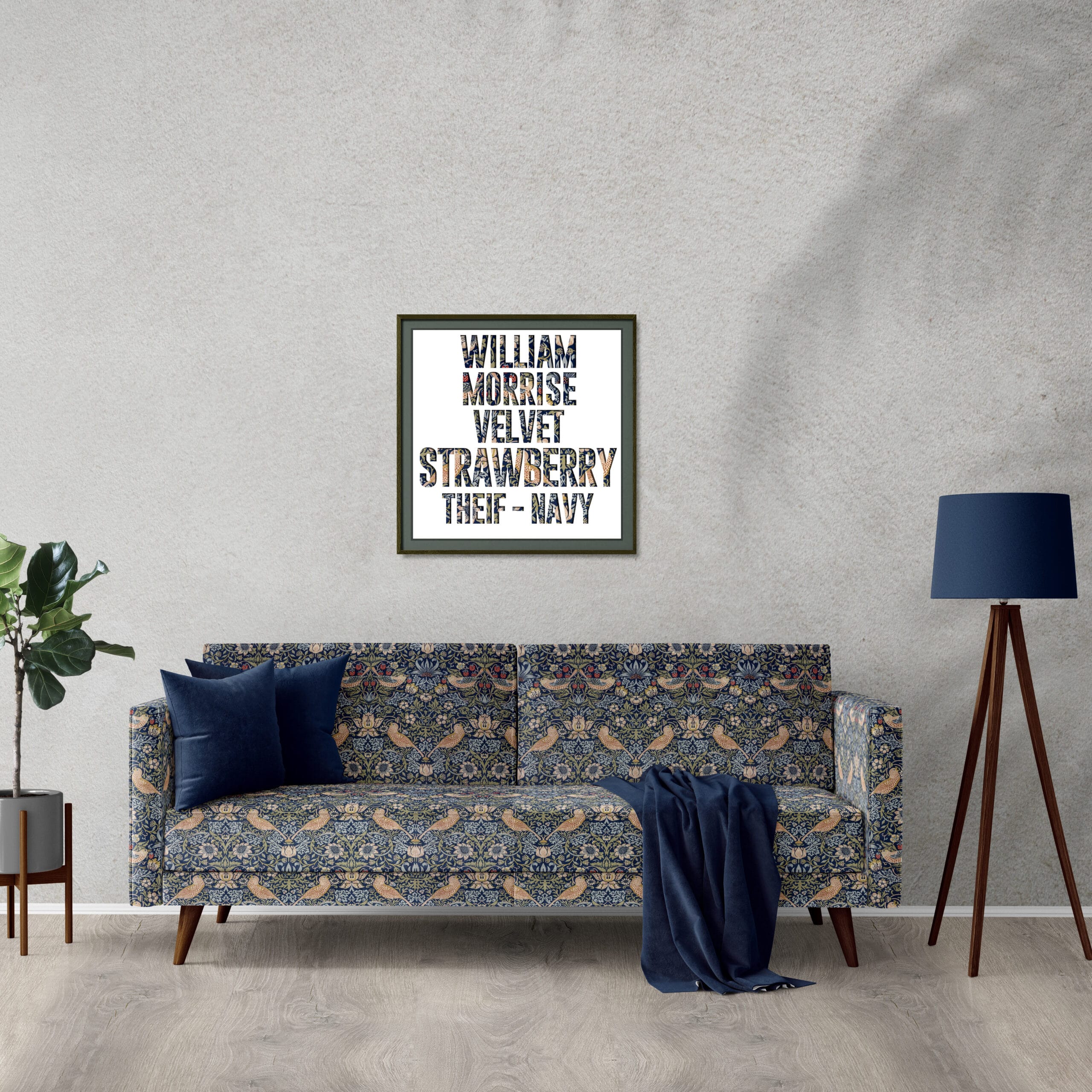 A stylish living room features a patterned blue sofa with two navy cushions and a draped throw. A framed print with text hangs above the sofa, complementing the minimalist decor. A tall lamp and a potted plant complete the setting.