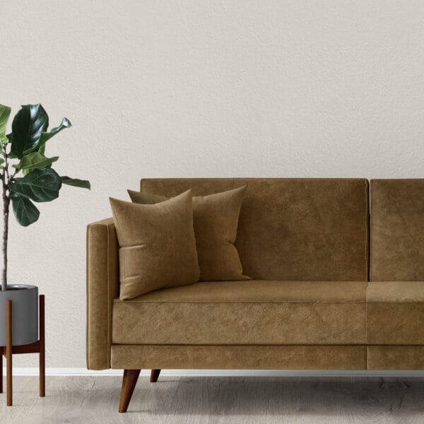 A minimalist living room with a brown suede sofa, two matching cushions, and a potted fiddle leaf fig plant in a gray planter. The neutral-toned wall and light wooden floor create a calm and modern ambiance.