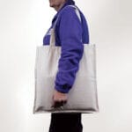 A person in a blue jacket carries the Eco-Friendly Canvas Tote Bag on their shoulder against a plain white background.